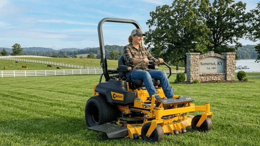 Person driving a zero turn mower across a wide lawn near a Somerset, Kentucky sign with fencing and rolling hills in the background.