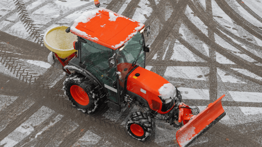 Tractor with a rear-mounted salt spreader applying material on icy pavement, illustrating how to choose the right salt spreader in Somerset, KY.