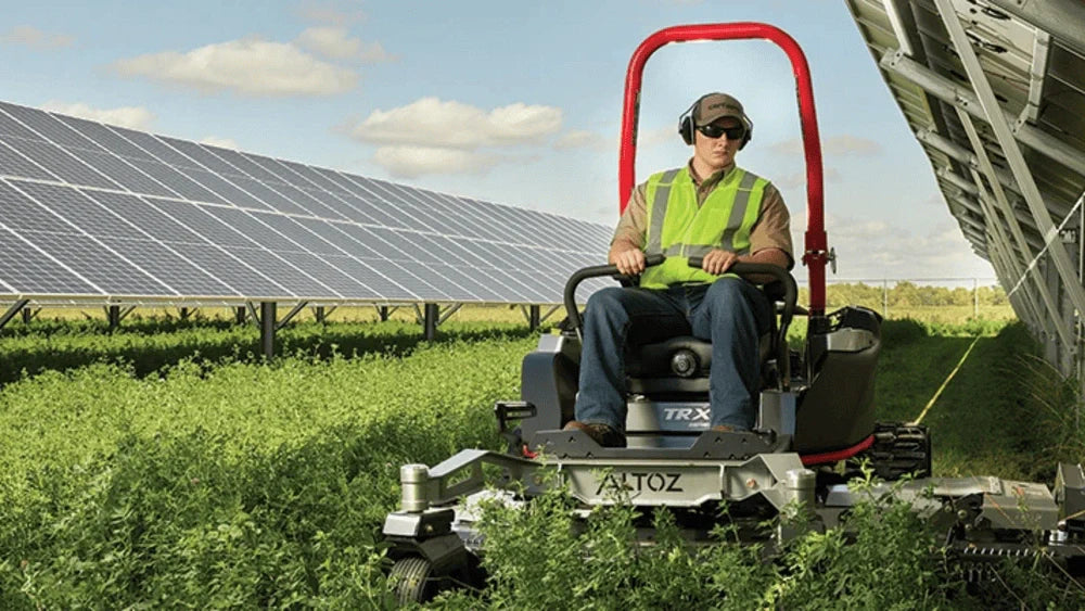 Operator using an Altoz TRX commercial tracked mower under solar panels, built for Kentucky lawn contractors.