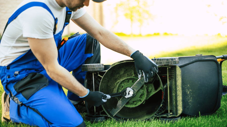Technician repairing a lawn mower blade and deck, showing common signs your lawn mower needs repairs and where to fix it in Somerset, KY.
